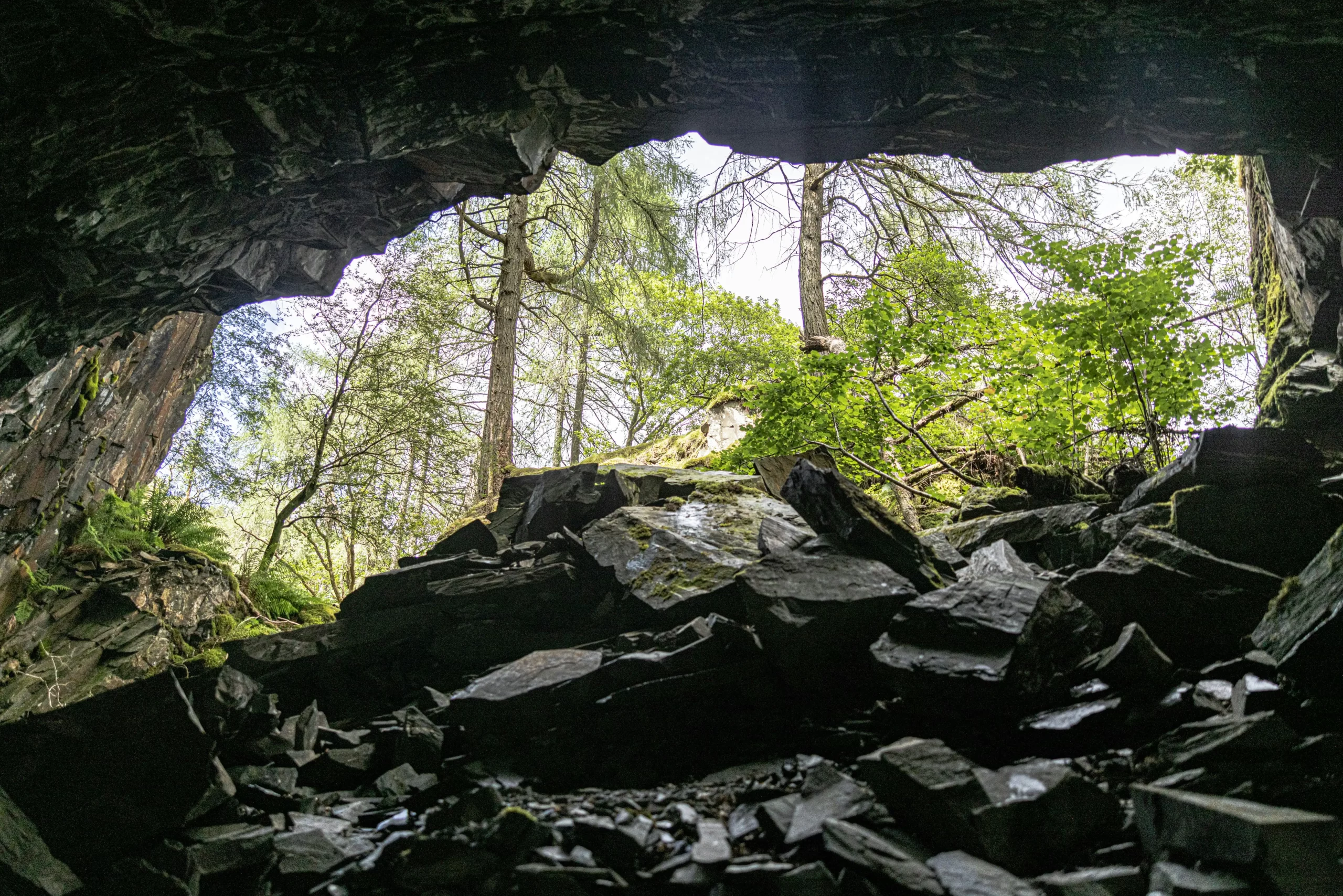 Interior de uma gruta em Ibitipoca, Minas Gerais, com rochas escuras e abertura iluminada que revela árvores e vegetação da serra.