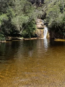 Lago dos Espelhos em Ibitipoca, Minas Gerais, com águas douradas e uma pequena cachoeira cercada por vegetação nativa.
