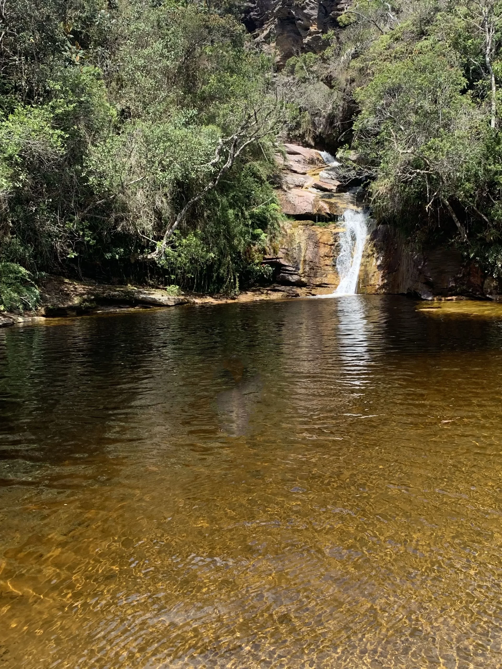 Lago dos Espelhos em Ibitipoca, Minas Gerais, com águas douradas e uma pequena cachoeira cercada por vegetação nativa.
