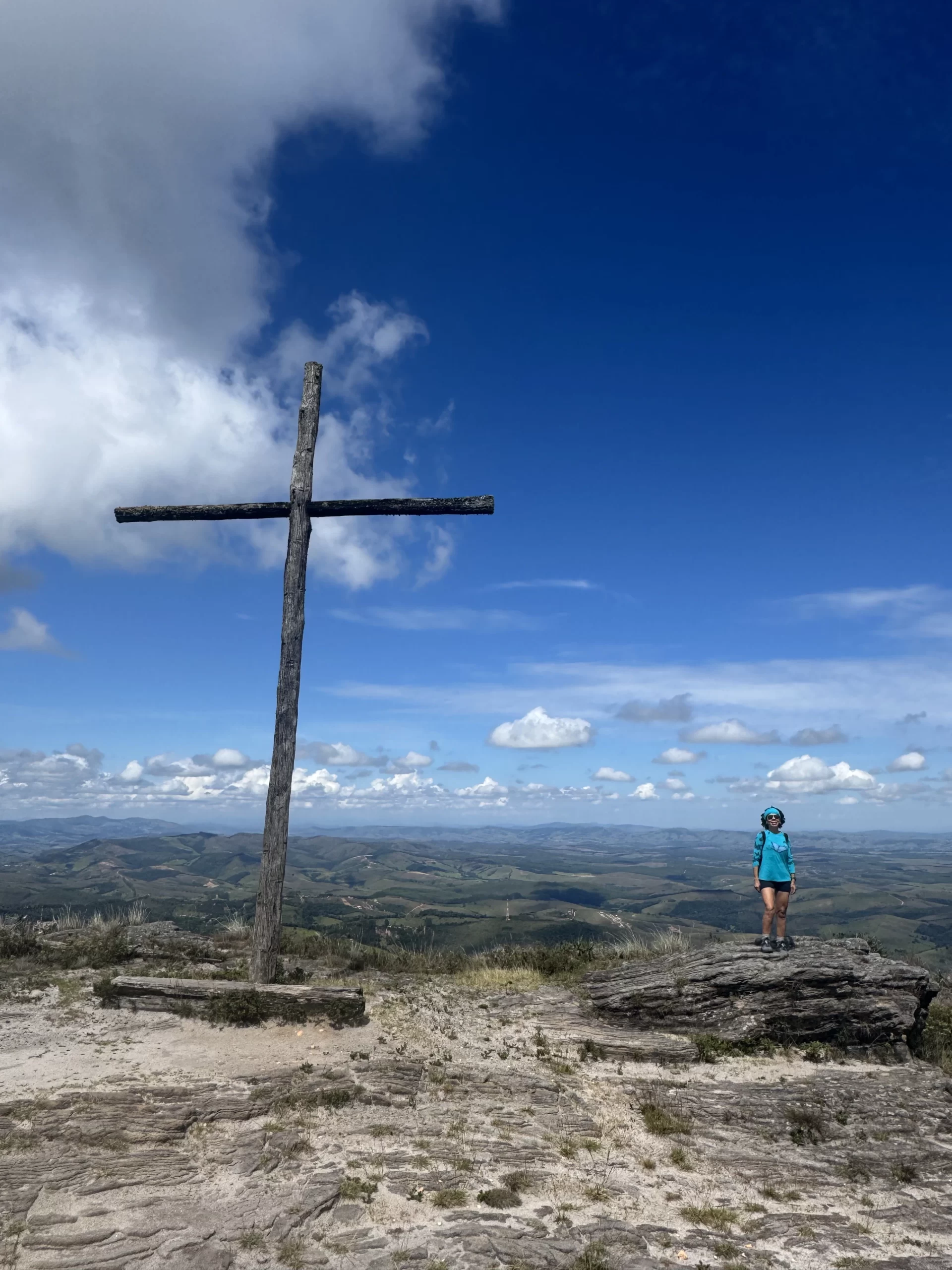 Pico do Cruzeiro em Ibitipoca, Minas Gerais, com uma grande cruz de madeira e vista ampla das montanhas sob o céu azul.